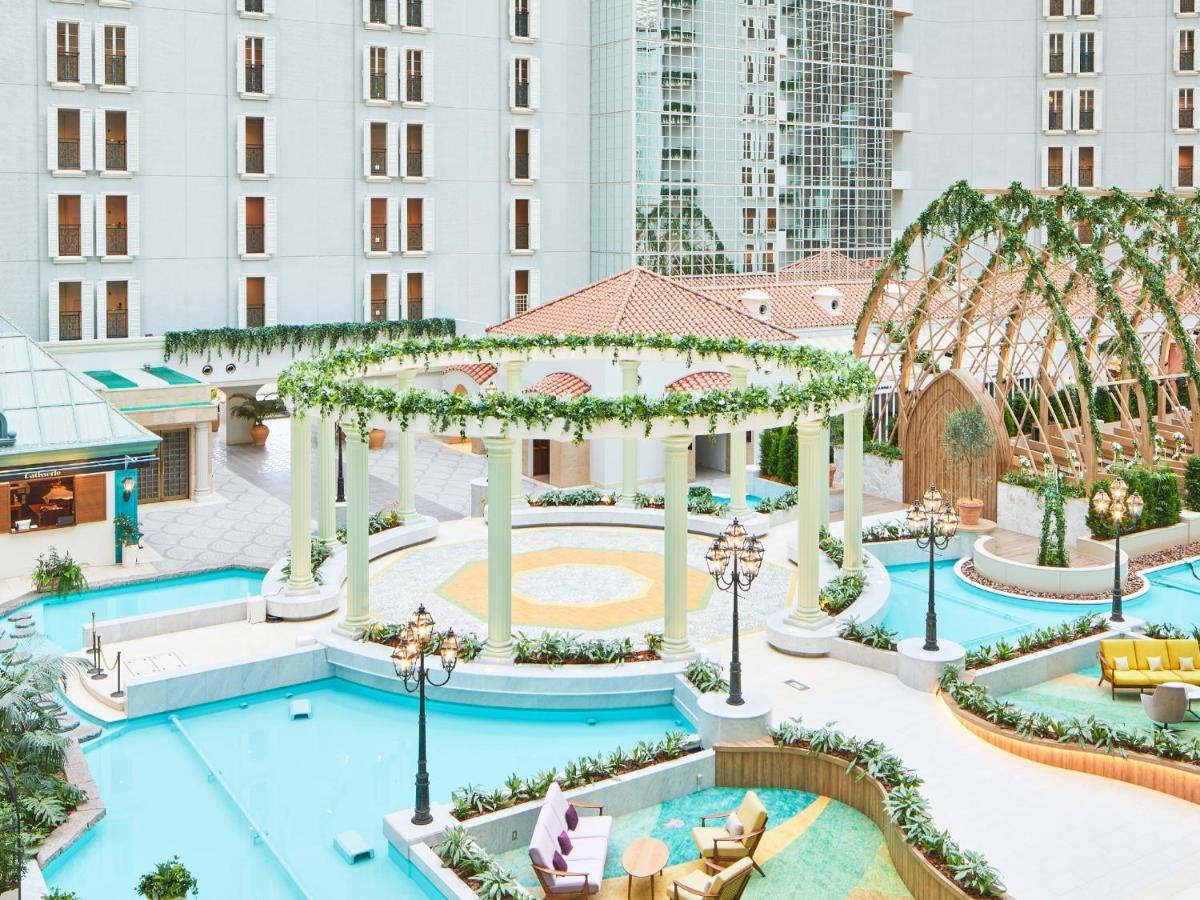 Grand Nikko Tokyo Bay Maihama Hotel Urajaszu Kültér fotó The photo shows a beautifully landscaped outdoor area, likely part of a resort or hotel. It features a central circular structure supported by white columns, decorated with greenery. Surrounding this structure are several swimming pools or water feat