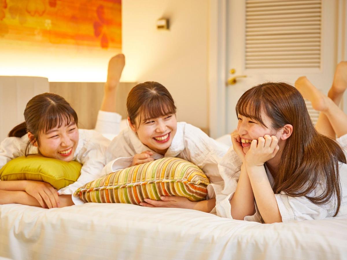Grand Nikko Tokyo Bay Maihama Hotel Urajaszu Kültér fotó The photo shows three young women lounging together in a cozy indoor setting. They are dressed in white robes and appear to be relaxed and enjoying each other's company. The women are lying on a bed, with two of them resting on their arms and the thi
