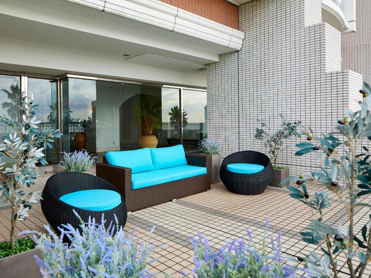 Grand Nikko Tokyo Bay Maihama Hotel Urajaszu Kültér fotó The image shows a stylish outdoor seating area. There is a brown couch with turquoise cushions, complemented by two matching round chairs nearby. The seating is arranged on a tiled patio, which is bordered by planters featuring lavender flowers and g