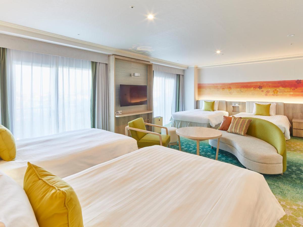 Grand Nikko Tokyo Bay Maihama Hotel Urajaszu Kültér fotó The photo shows a modern hotel room that features two large beds covered with white bedding and decorative pillows. There is a contemporary, curved sofa in a light color, along with a round table in the middle. The room has large windows that allow n