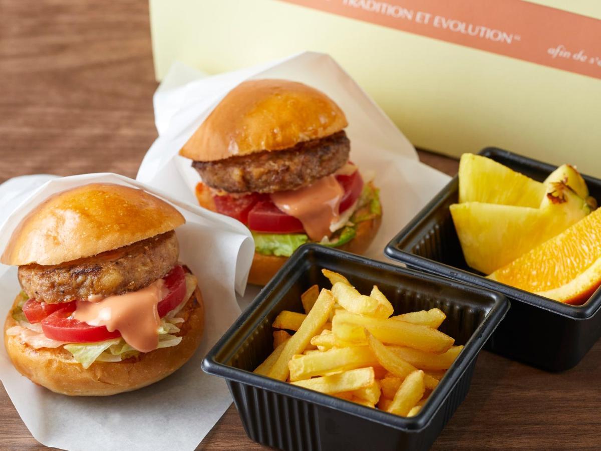Grand Nikko Tokyo Bay Maihama Hotel Urajaszu Kültér fotó The photo shows two small burgers placed on a white background, each with a golden-brown bun, a fried patty, lettuce, tomato, and a creamy sauce. Alongside the burgers, there are two containers: one holding a serving of french fries and the other con