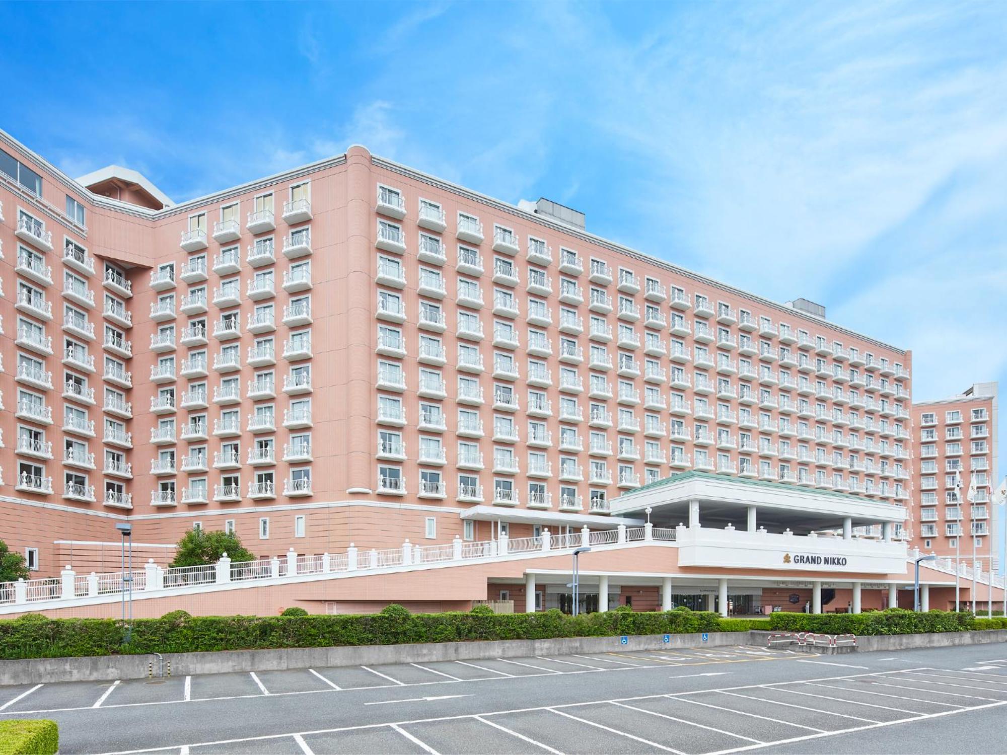 Grand Nikko Tokyo Bay Maihama Hotel Urajaszu Kültér fotó The photo shows a large, multi-story hotel building, characterized by its pink facade and modern architectural design. The structure features numerous windows and a spacious entrance area, complemented by a canopy. In front of the hotel, there is a p