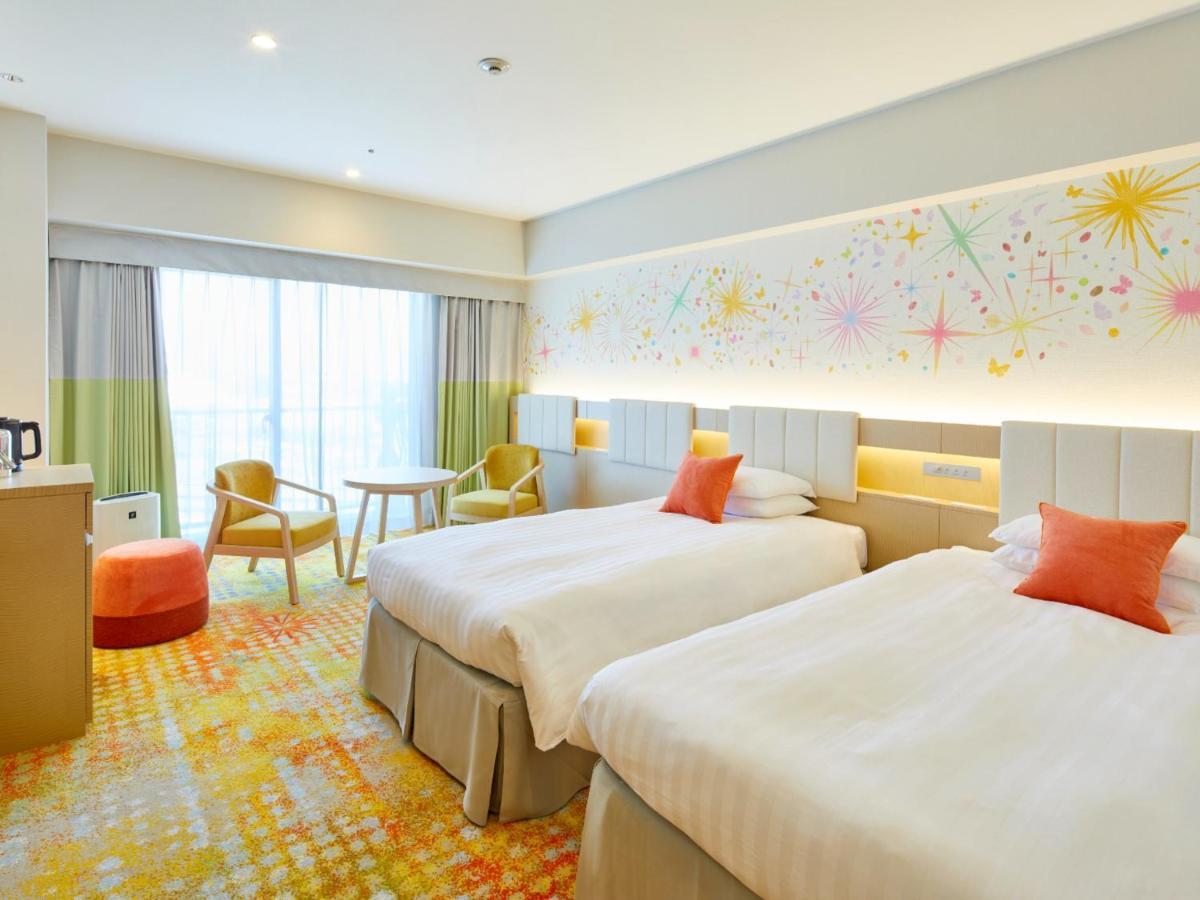 Grand Nikko Tokyo Bay Maihama Hotel Urajaszu Kültér fotó The photo shows a modern hotel room featuring two twin beds with light-colored bedding and decorative orange cushions. There is a vibrant, colorful carpet on the floor, and the walls are adorned with playful designs, including bursts of color. A larg