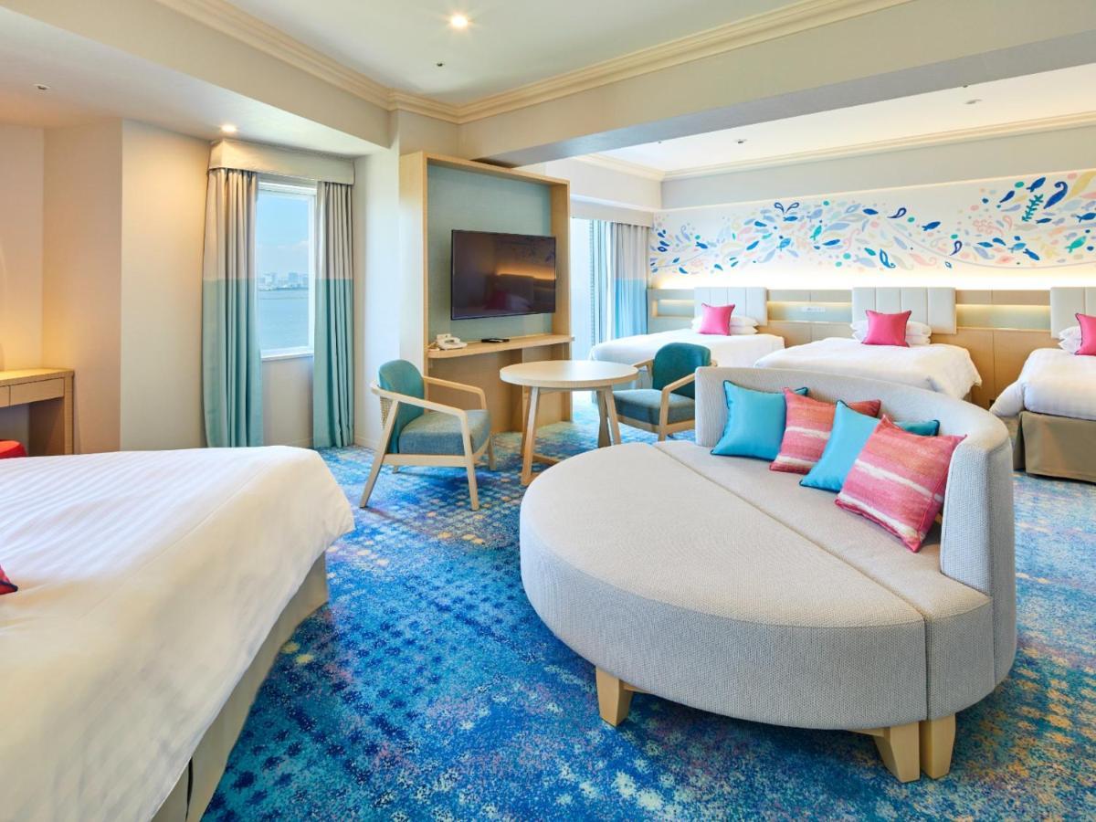 Grand Nikko Tokyo Bay Maihama Hotel Urajaszu Kültér fotó The photo shows a modern hotel room featuring a spacious layout with multiple beds. There is a large, curved sofa with colorful cushions in the center, adding a contemporary touch to the design. The room has large windows allowing natural light to fi