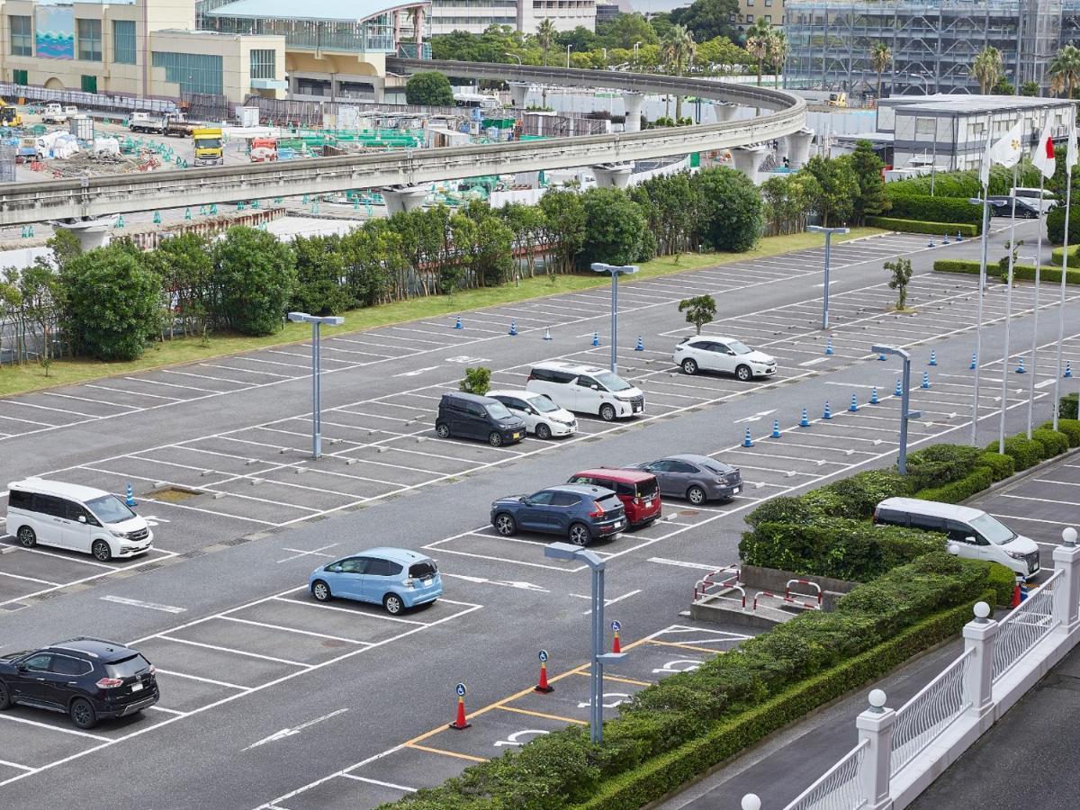 Grand Nikko Tokyo Bay Maihama Hotel Urajaszu Kültér fotó The photo shows a partially empty parking lot with several parked cars. In the foreground, there are a few vehicles, including a blue car and a white one. The lot has clearly marked parking spaces, and there are some trees and shrubs along the sides.