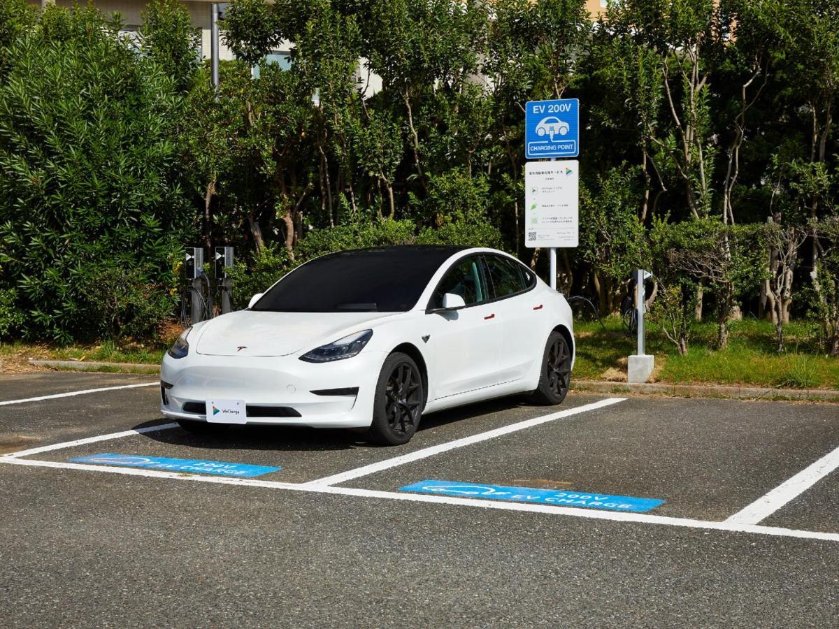 Grand Nikko Tokyo Bay Maihama Hotel Urajaszu Kültér fotó The photo shows a white electric car parked in an EV (electric vehicle) charging spot. The car has a sleek design with black wheels and tinted windows. In the background, there are green shrubs and trees, indicating a natural or landscaped environmen