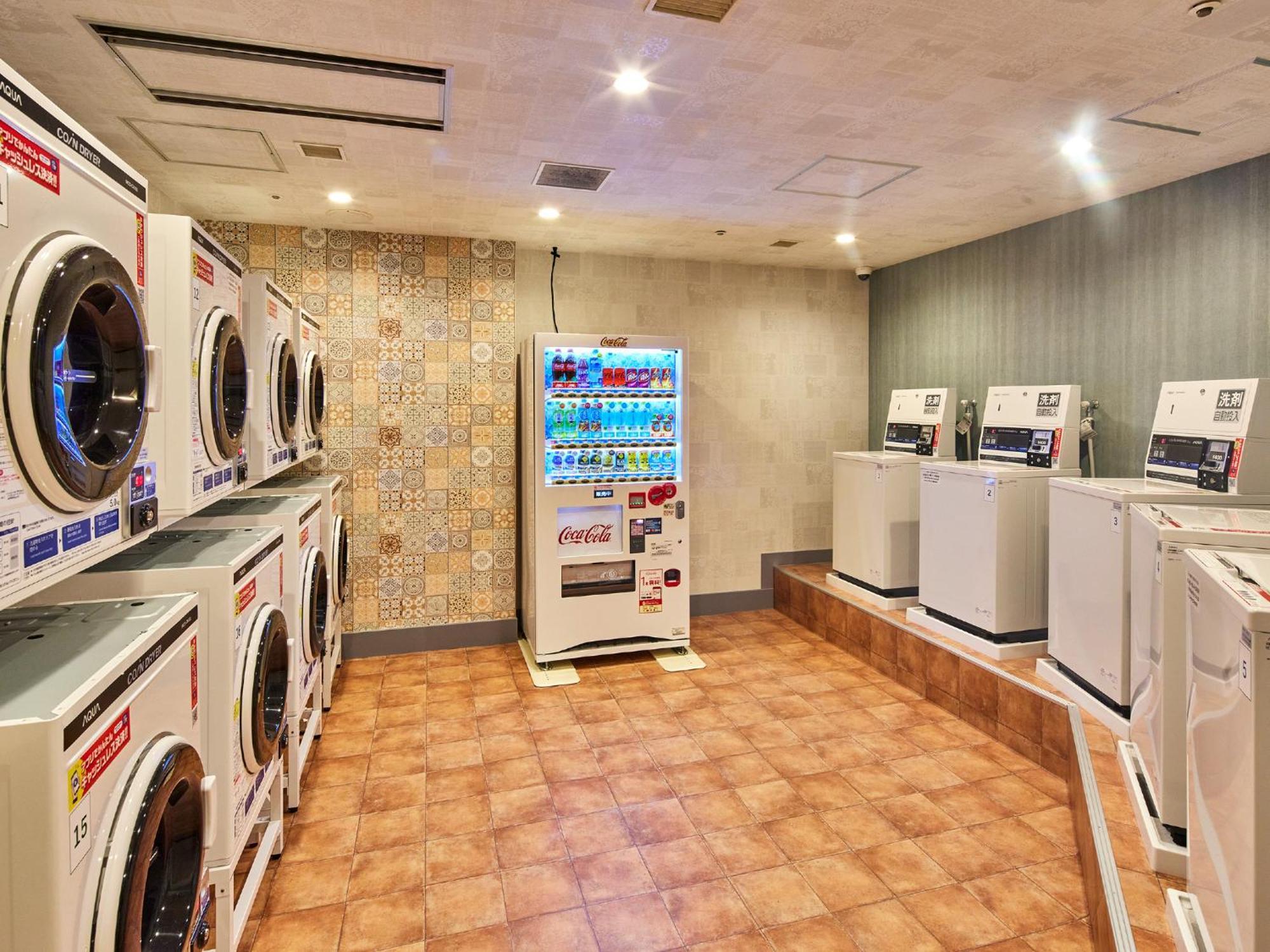 Grand Nikko Tokyo Bay Maihama Hotel Urajaszu Kültér fotó The photo shows a laundry room equipped with several washing machines and dryers. On the left side, there are multiple front-loading washing machines arranged in a row, and on the right side, there are dryers. In the center, there is a vending machin
