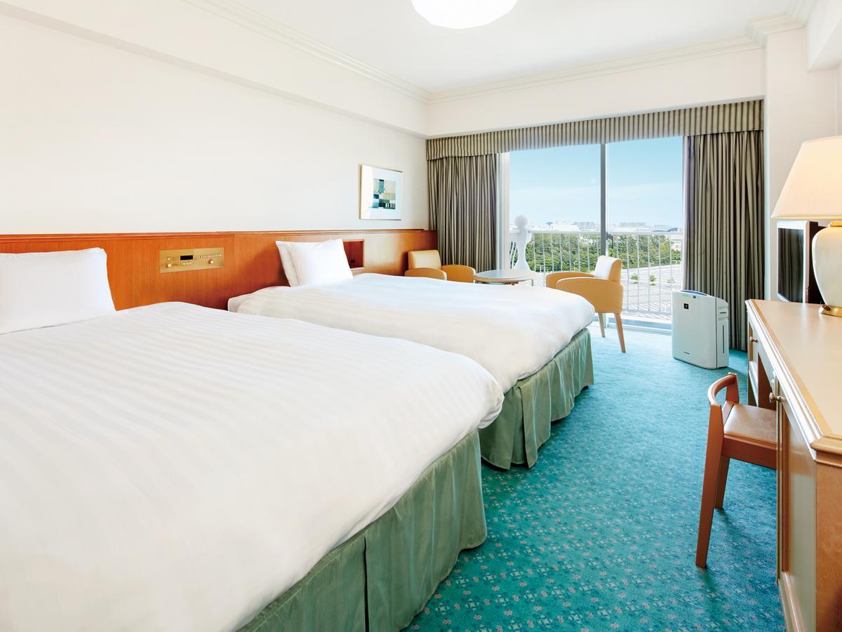 Grand Nikko Tokyo Bay Maihama Hotel Urajaszu Kültér fotó The photo shows a hotel room featuring two twin beds with white bedding. The walls are painted in light colors, and there’s a window that offers a view outside, letting in natural light. A small table and chairs are visible near the window, as well a