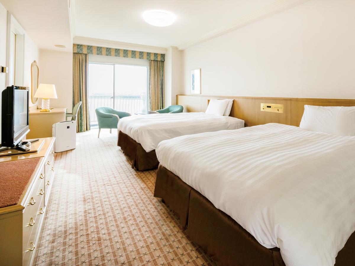 Grand Nikko Tokyo Bay Maihama Hotel Urajaszu Kültér fotó The photo shows a hotel room featuring two large beds with white bedding and brown bases. There's a light-colored carpet on the floor, and the room is brightly lit. To one side, there is a television on a stand and a small white refrigerator. A desk 